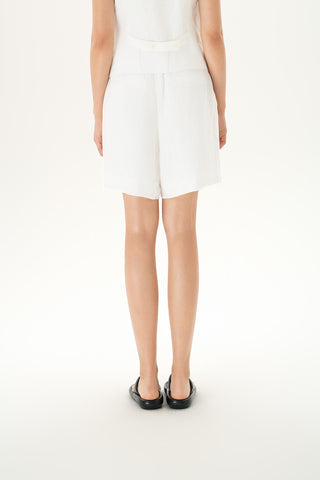Woman wearing tailored white linen shorts with button closure and pleats
