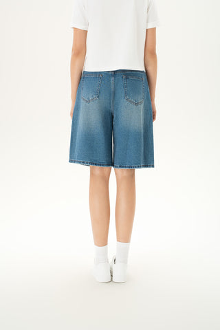 Woman wearing wide-leg denim Bermuda shorts in a mid-rise, medium-light wash