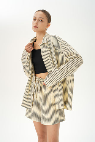 Woman wearing a beige crinkled striped shirt and matching striped shorts on a white background