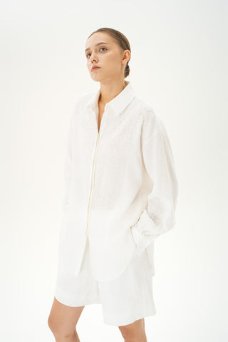 Woman wearing oversized linen button-down shirt with gathered sleeves and beaded details