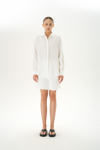 Woman wearing oversized linen button-down shirt with gathered sleeves and beaded details