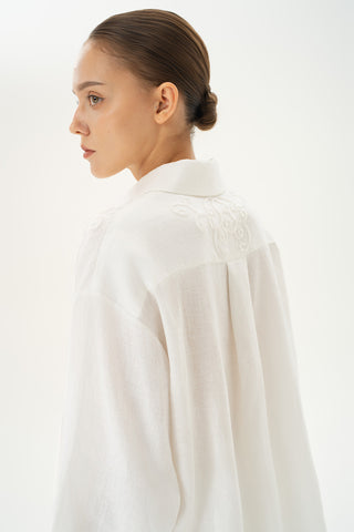 Woman wearing oversized linen button-down shirt with gathered sleeves and beaded details