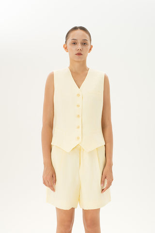 Woman wearing a light yellow tailored linen vest with button-front closure and faux pockets