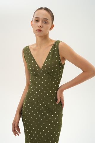Woman wearing a bias-cut silk midi dress with a V-neckline and gathered bust in olive green with beige polka dots. 