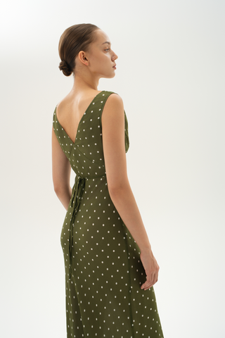 Woman wearing a bias-cut silk midi dress with a V-neckline and gathered bust in olive green with beige polka dots. 