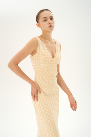 Woman wearing a bias-cut silk midi dress with a V-neckline in light beige with white polka dots