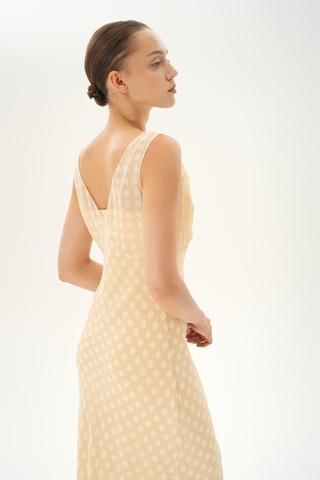 Woman wearing a bias-cut silk midi dress with a V-neckline in light beige with white polka dots